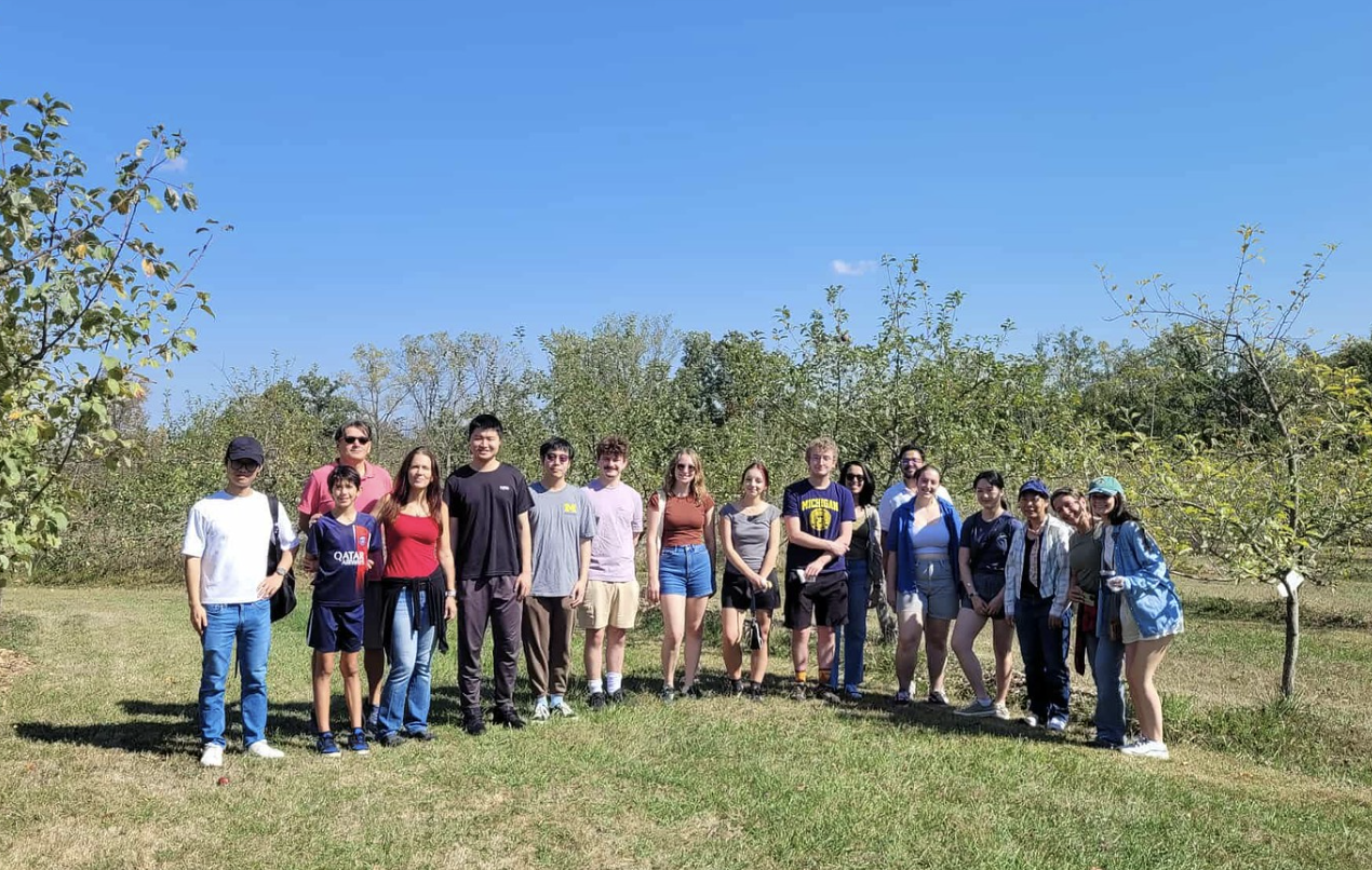 Veronica standing with people from michigan AI lab at an apple orchard (the trees don't have any apples on them)