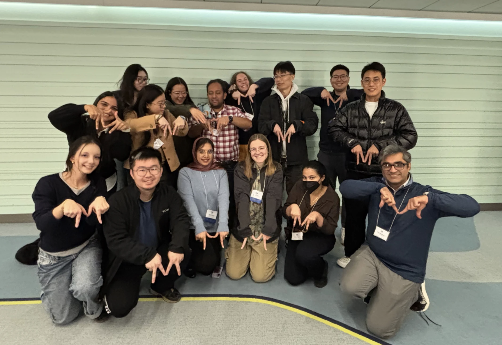 group photo in the hallway of the ASSETS conference, depicting two rows of people. back row, from left to right:  Shalini Madan, Xuanyu Liu, Xinyun Cao, Rosiana Natalie, Venkatesh Potluri, Ellie Seehorn, Liang-Yuan Wu, Jeremy Huang, Ruei-Che Chang. bottom row (kneeling): Veronica Pimenova, Yao Lyu, Hira Jamshed, Kaia Newman, Rahaf Alharbi, Mustafa Naseem